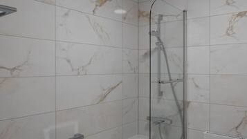 Un baño moderno con ducha envuelta en vidrio, una bañera blanca y paredes con diseño de mármol.