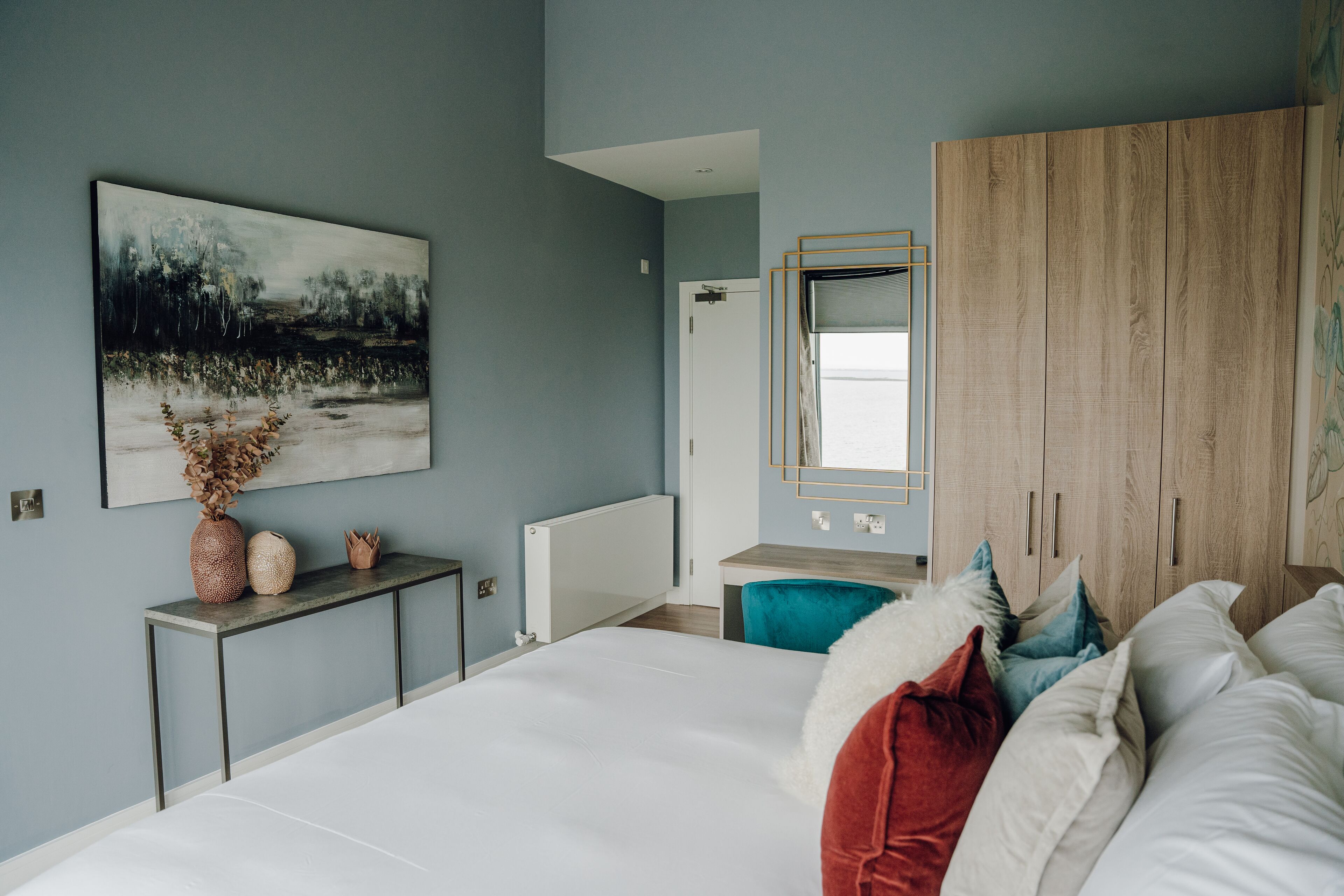 Un dormitorio con una cama grande, un armario de madera, un escritorio con silla, un radiador y un cuadro en la pared.
