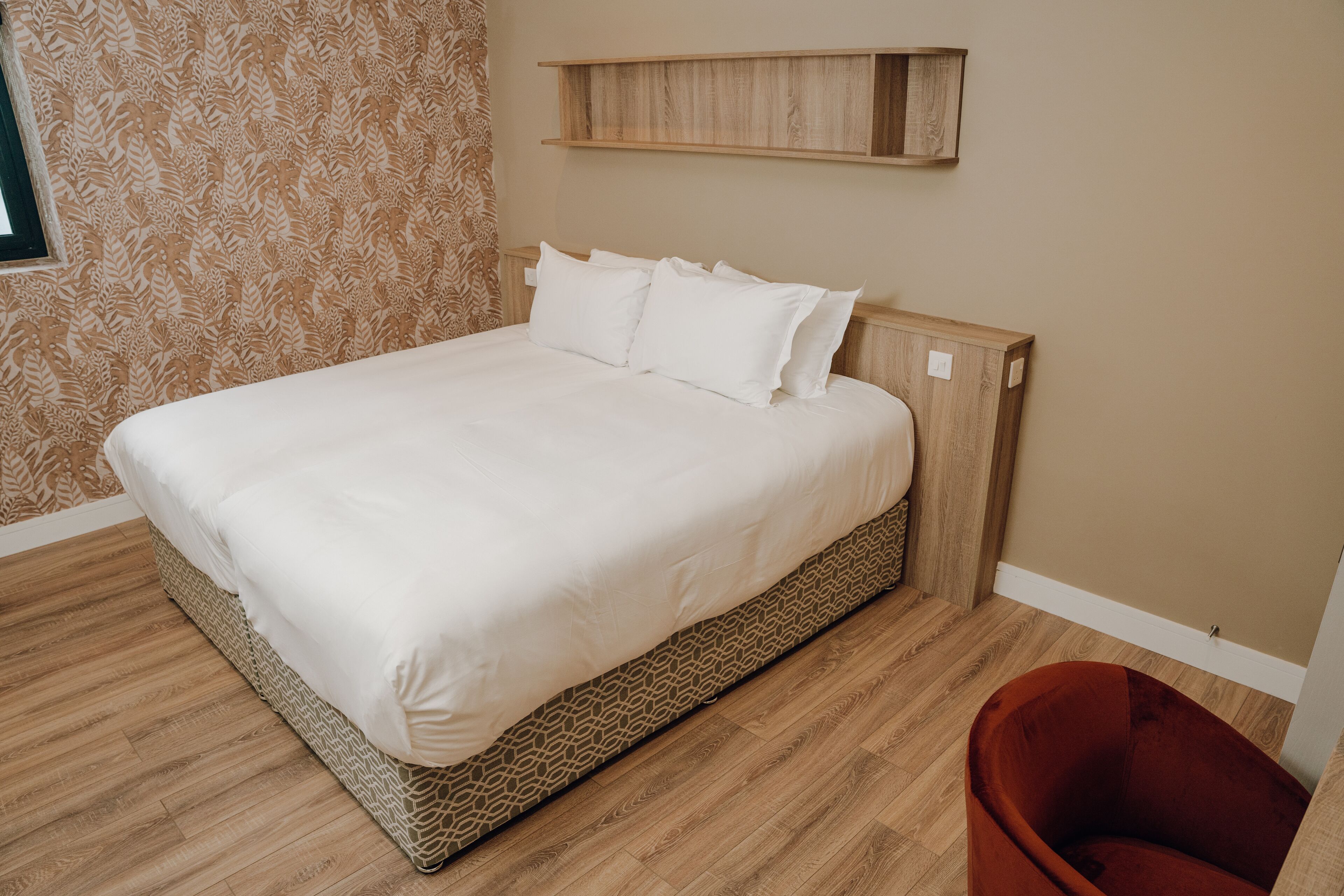 Una cama bien hecha con cabecera de madera, pared con diseño y un pequeño estante encima.