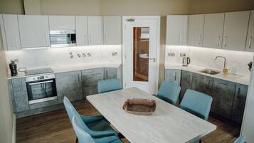 A modern kitchen with grey cabinets, a built-in oven, and a dining area with a light-colored table and blue chairs.