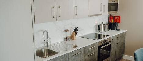 A modern kitchen with white and grey cabinetry, a stainless steel sink, a built-in oven, and a coffee maker.