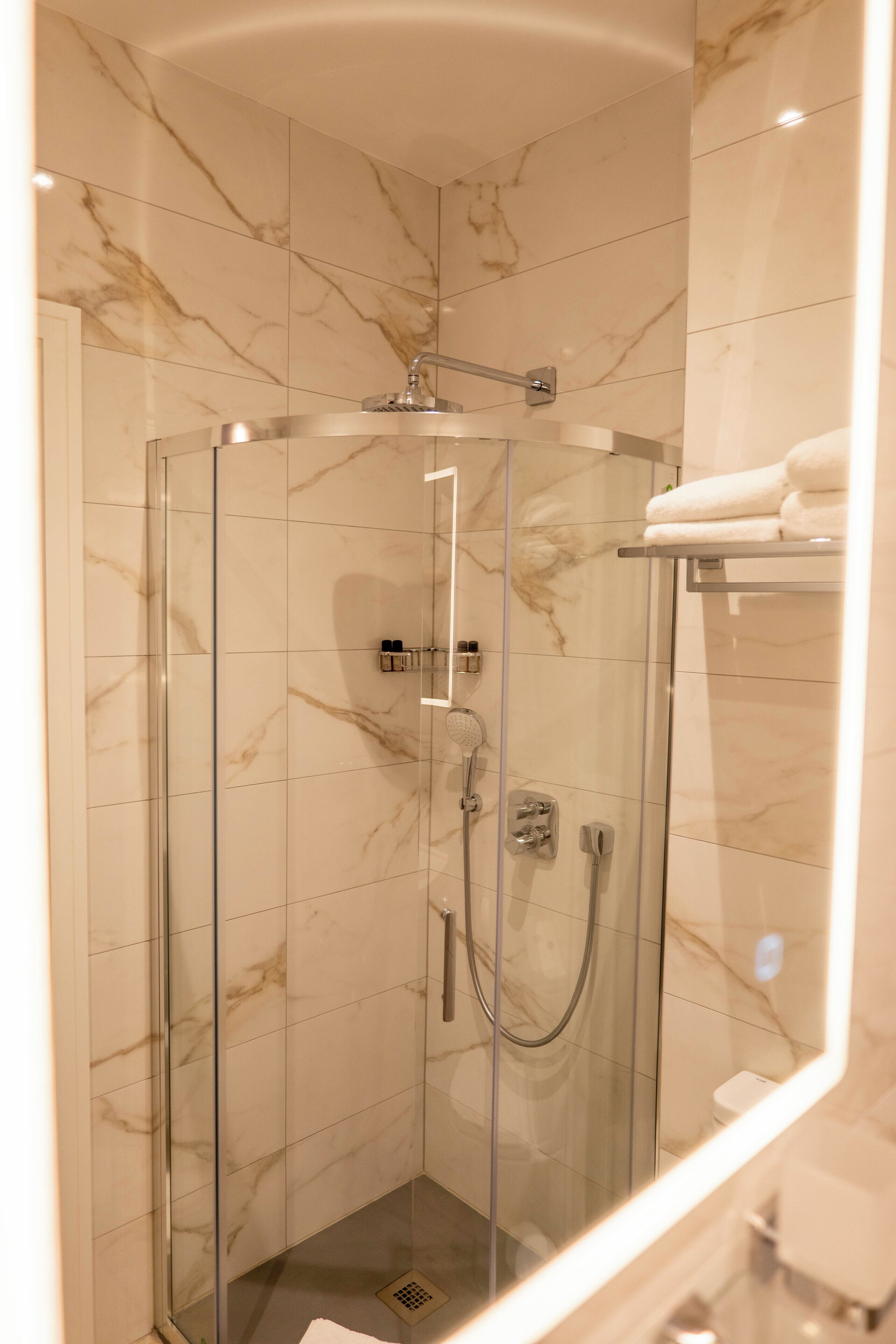 Een douche met glazen wand, een handdouche, een wandmengkraan en bedieningspaneel.