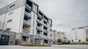 A modern multi-story building with balconies, a stone facade, and a paved courtyard.