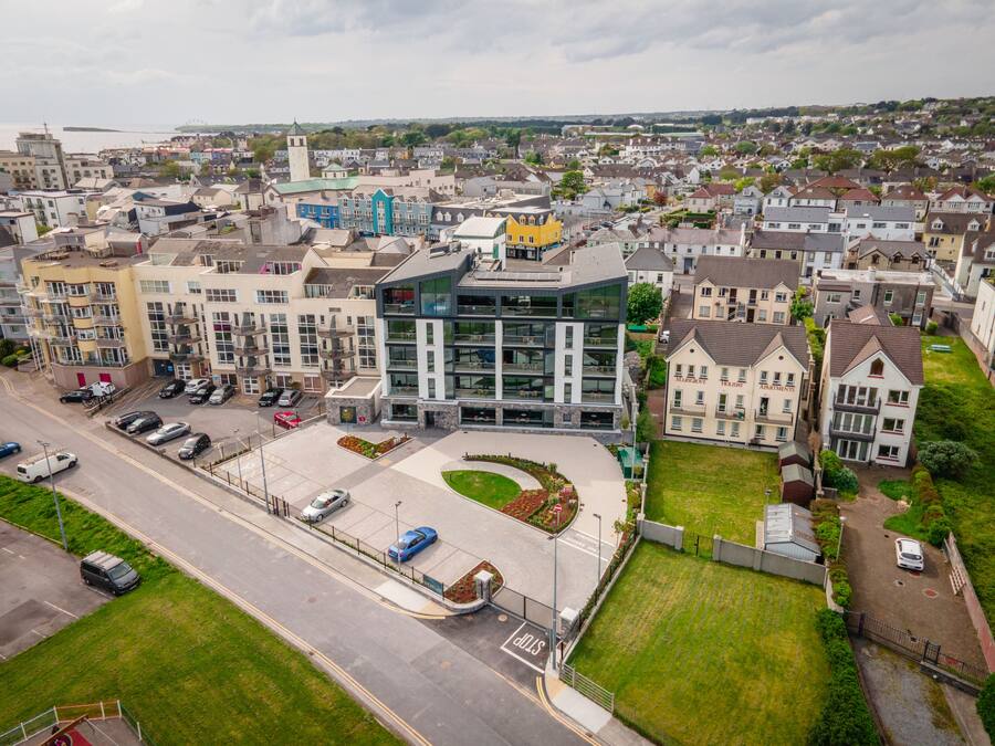 An aerial view of a residential area with modern apartment buildings, a parking lot, and a road.