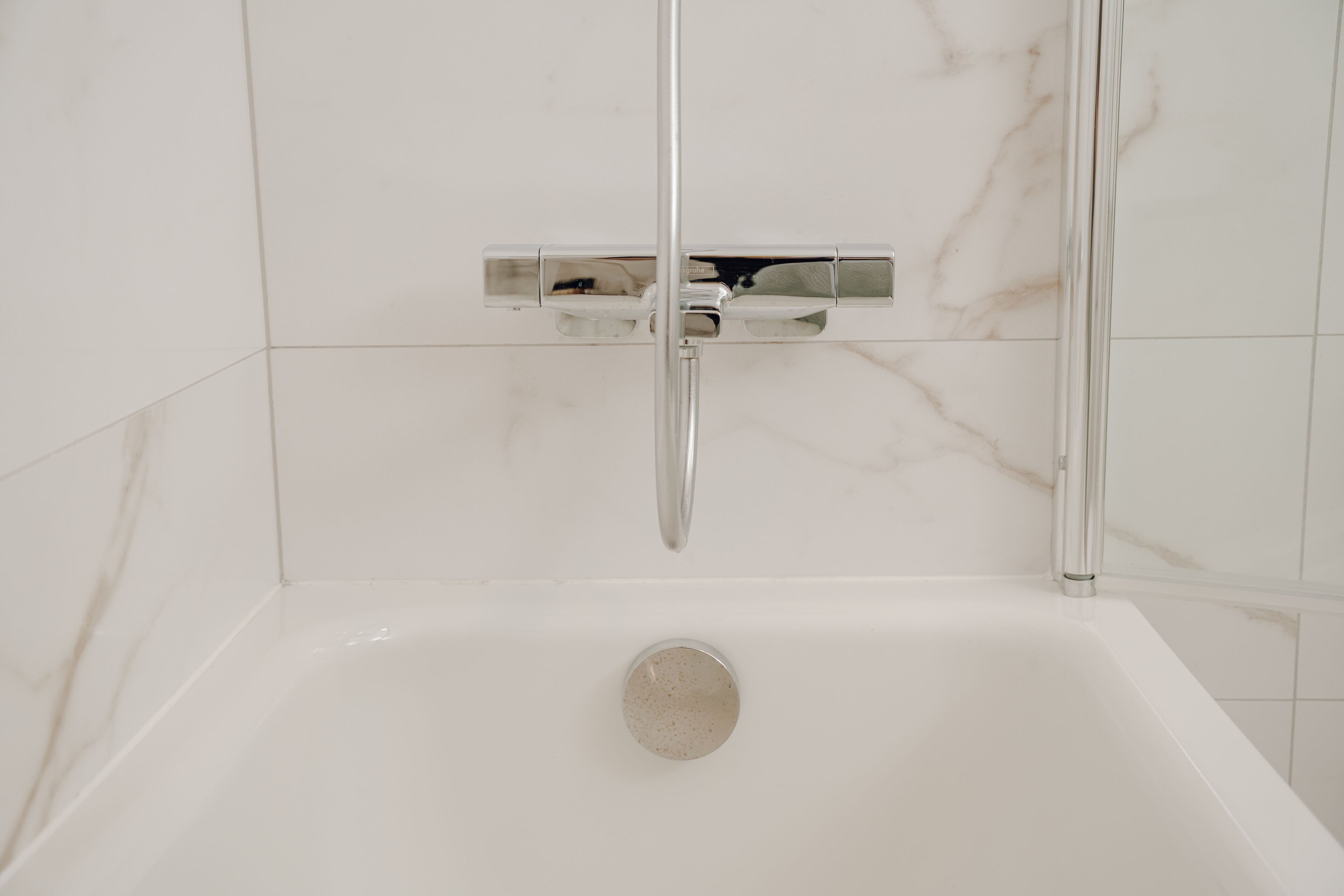 Un baño moderno con una bañera blanca, grifería cromada y baldosas de mármol.