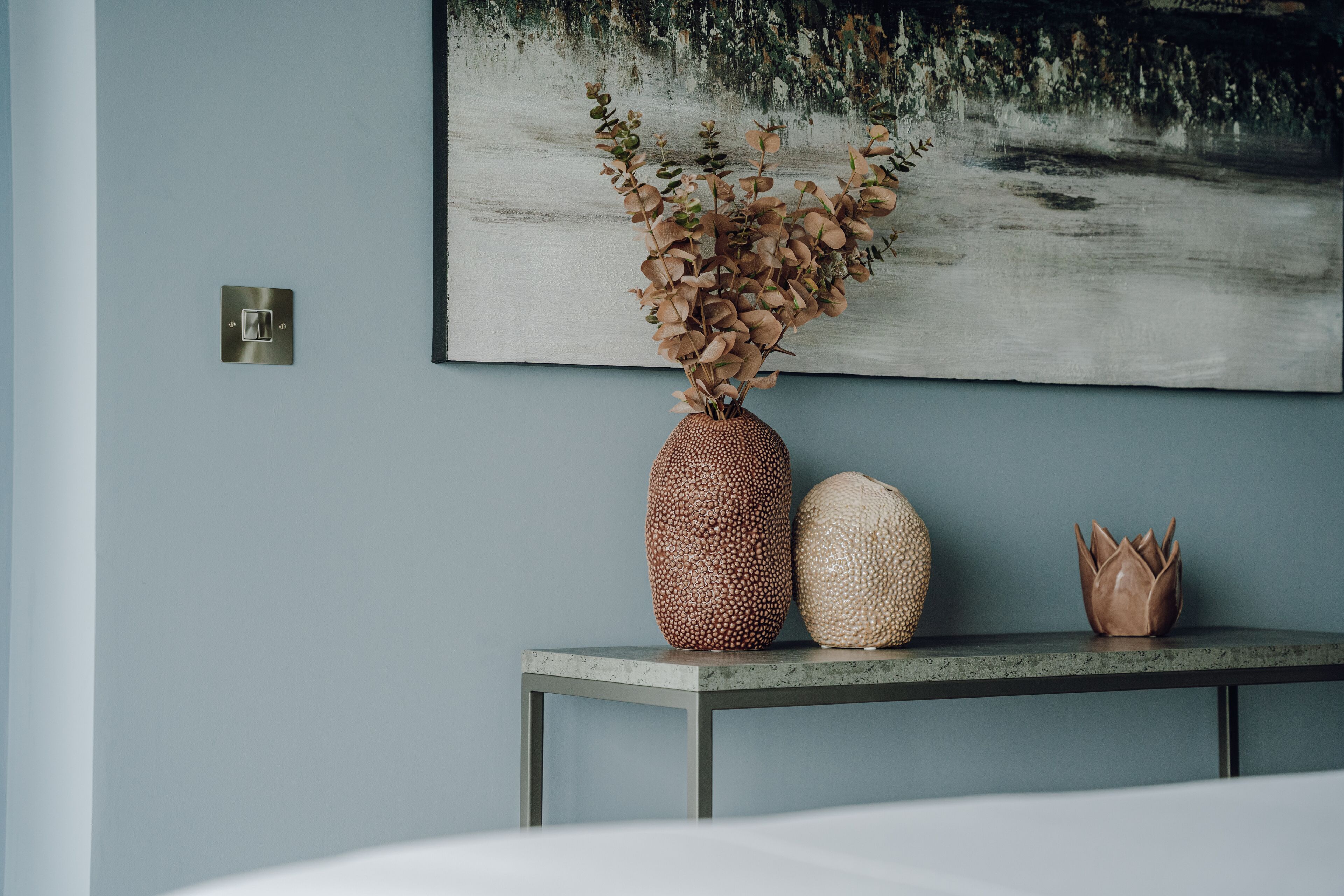 A room with a bed, a table with decorative items, and a painting on the wall.