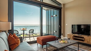 A modern living room with a sofa, coffee table, and a TV. There is a balcony with a view of the sea. - Shoreline Apartments (Galway)