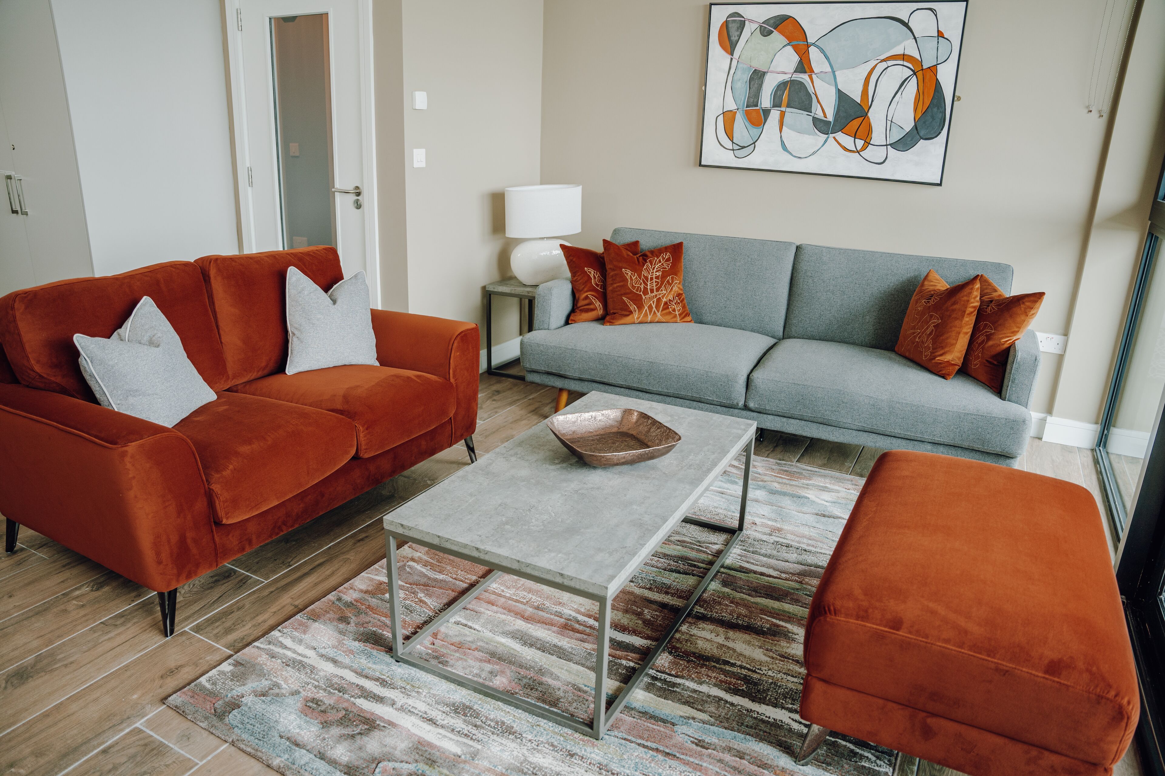 A living room with a grey sofa, orange armchairs, a coffee table, and a patterned rug.