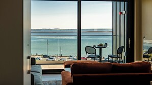 A room with a large sliding glass door leading to a balcony with a view of the sea and a parking area. - Shoreline Apartments (Galway)