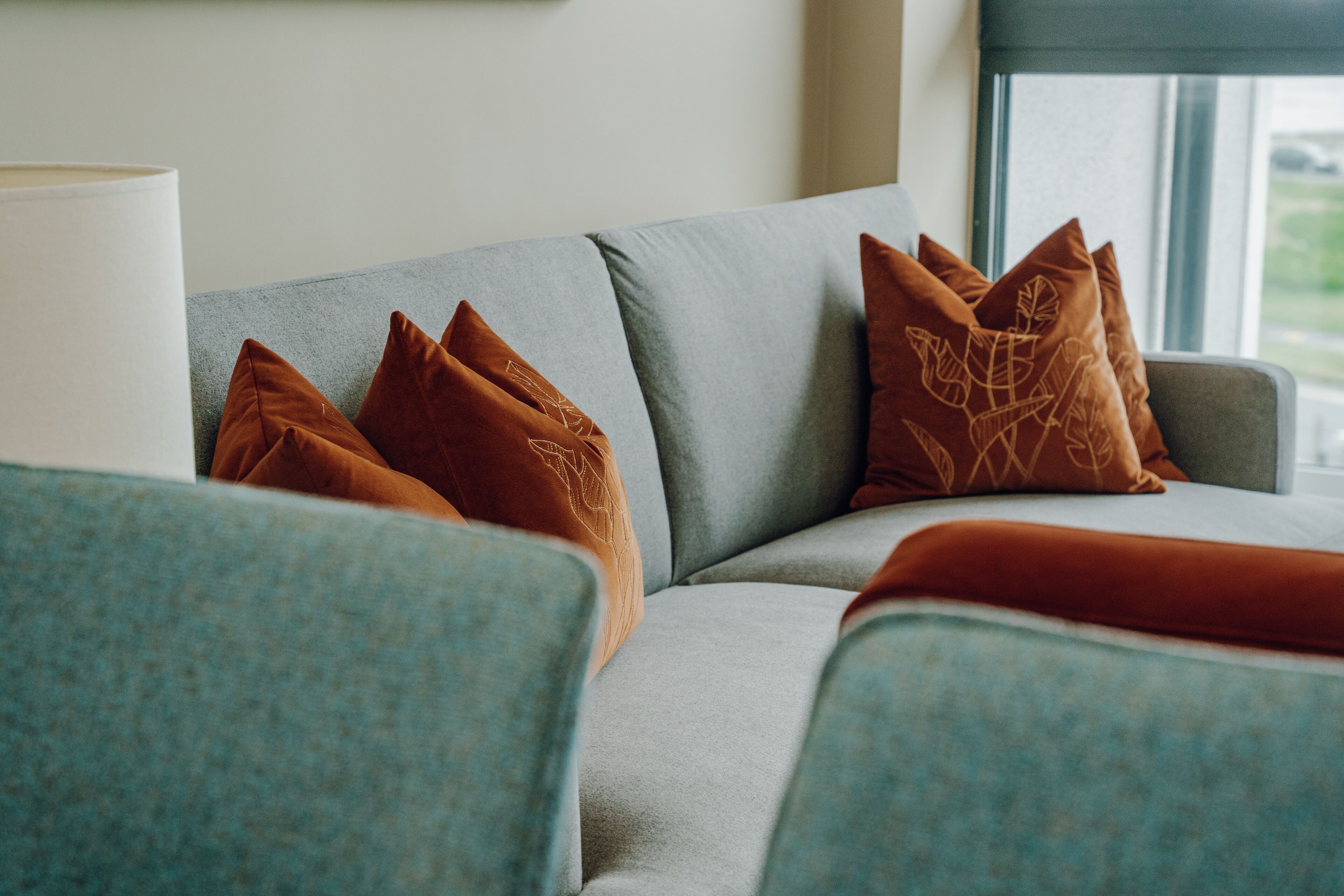A modern living room with a grey sofa, brown patterned cushions, and a blue armchair.