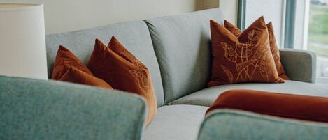 A modern living room with a grey sofa, brown patterned cushions, and a blue armchair.