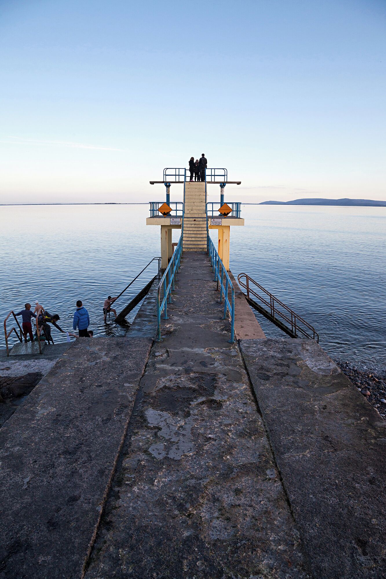 A pier leading to a small platform with railings and a sign.