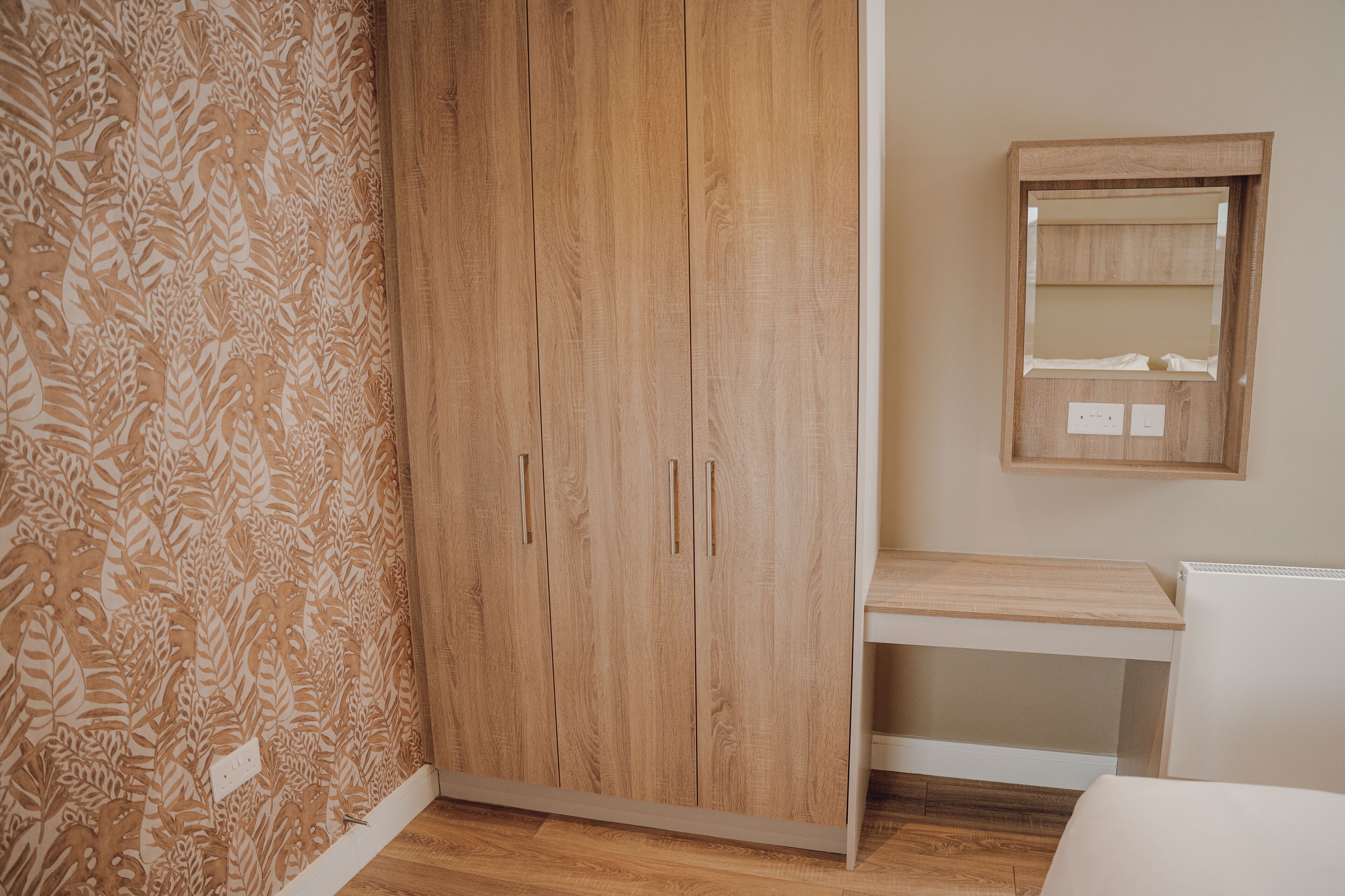 A room with a wooden wardrobe, a small desk, and a mirror on the wall.