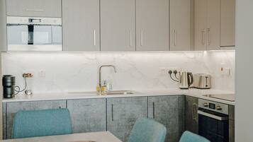 A modern kitchen with grey cabinets, a white marble backsplash, a built-in oven, a coffee maker, and a kettle.