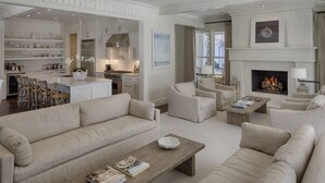Een ruime woonkamer met een open haard, een keuken achterin en een eethoek met stoelen.