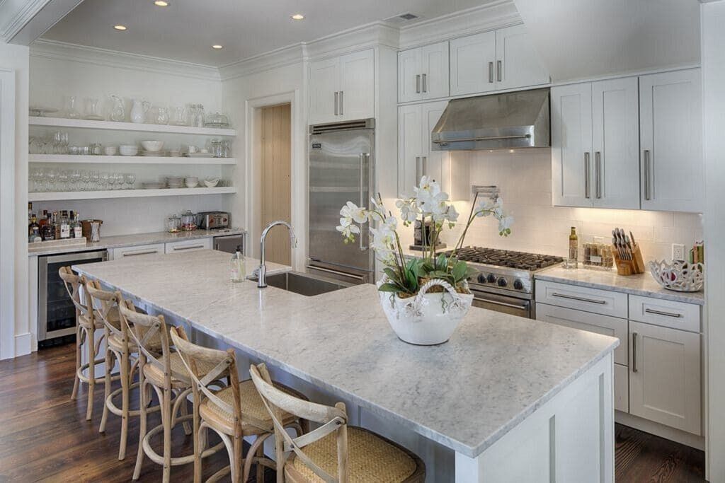 A modern kitchen with white cabinetry, a large island with bar stools, a stainless steel range hood, and a built-in oven.