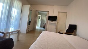 A hotel room with a bed, a TV mounted on the wall, a chair, and a desk.