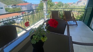 A balcony with a potted plant, two wicker chairs, and a view of a hillside with houses.