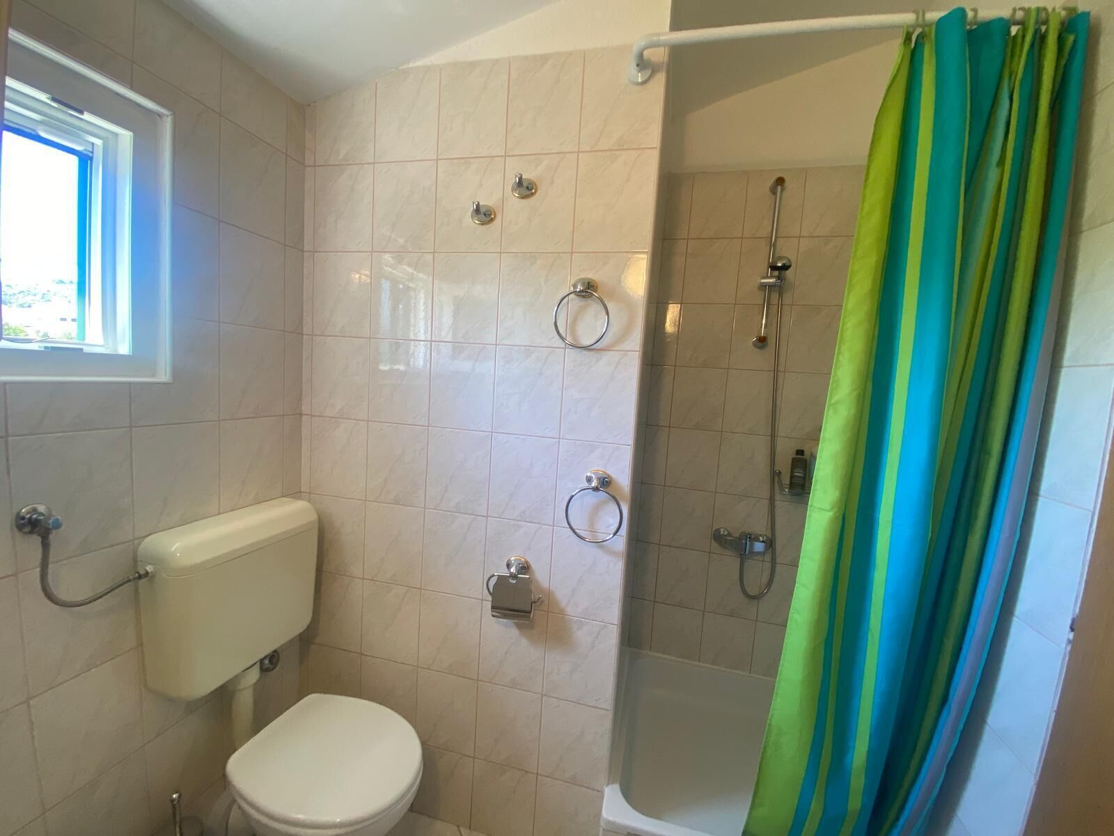 Une salle de bain avec des toilettes, une douche dotée d’une porte en verre et une fenêtre.