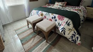 A bedroom with a bed, two nightstands, a ceiling fan, a window with blinds, a rug, and a painting on the wall. - Sugar Beach-C16 Unique in the best way. Just updated be first to enjoy upgrades. (Panama City)
