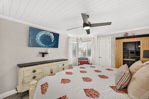 Ein Schlafzimmer mit Bett, Deckenventilator, Wand-Fernseher und einem großen Fenster mit Jalousien.