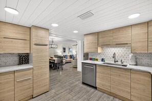 A modern kitchen with wooden cabinetry, a dishwasher, and a dining area with a table and chairs. - Sugar Beach-C16 Unique in the best way. Just updated be first to enjoy upgrades. (Panama City)