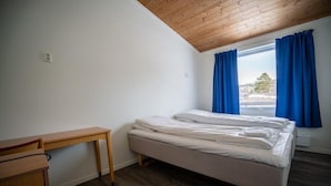 Une petite pièce, bien rangée, avec un lit simple, un bureau en bois et une fenêtre ornée de rideaux bleus.