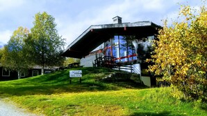Un bâtiment moderne à la façade vitrée, une enseigne indiquant un motel, et une pente herbeuse menant à l’entrée.