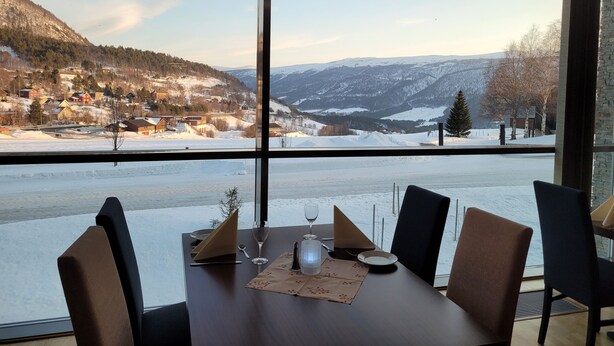 Une table à manger avec des chaises, donnant sur un paysage enneigé grâce à de grandes fenêtres.