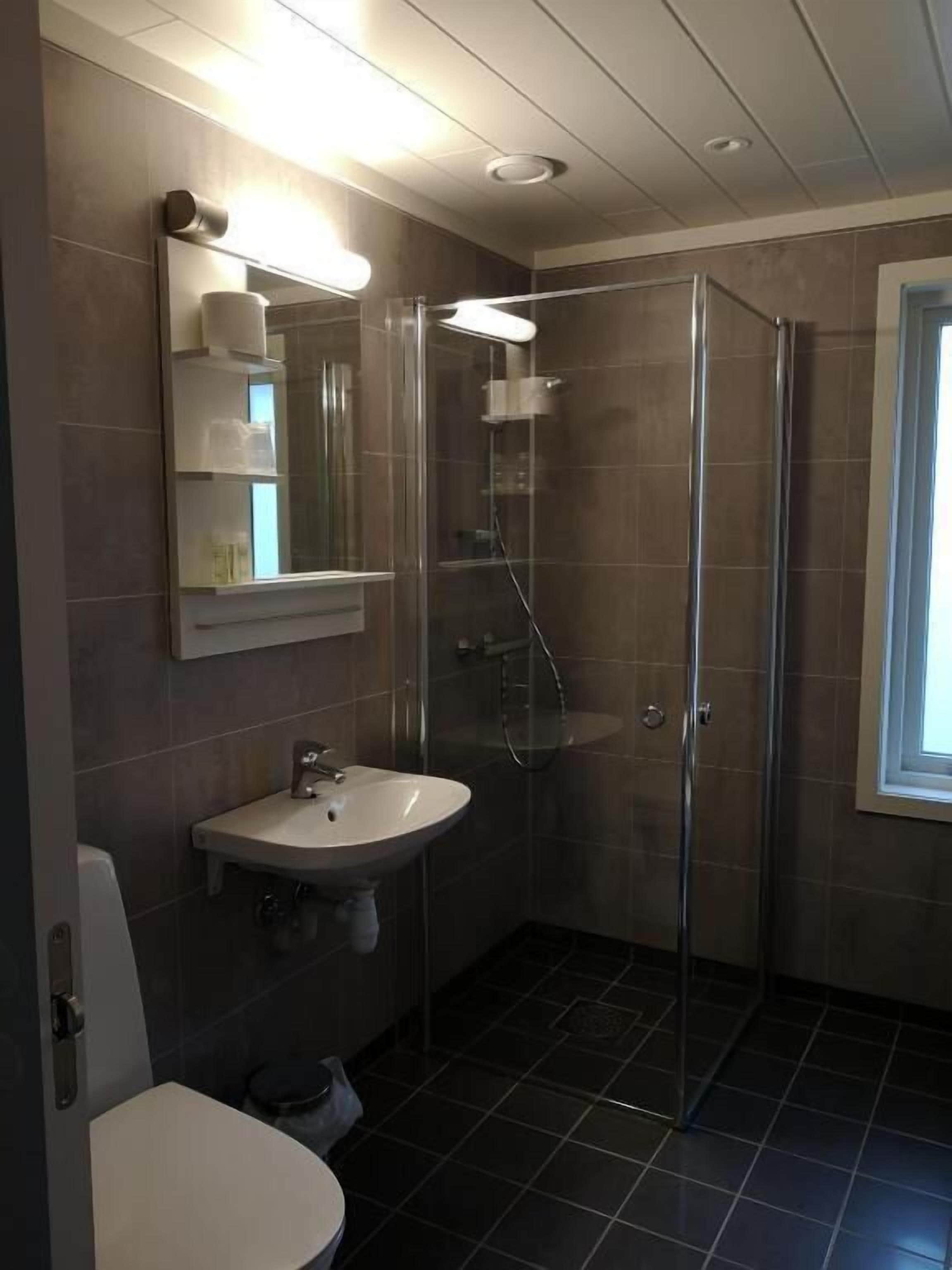 A modern bathroom with a glass-enclosed shower, a white sink, and a mirror with shelves.