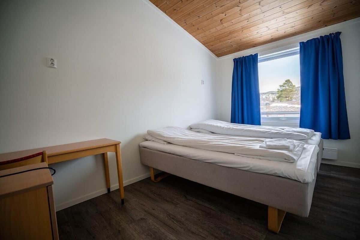 A room with a bed, a desk, and a window with curtains.
