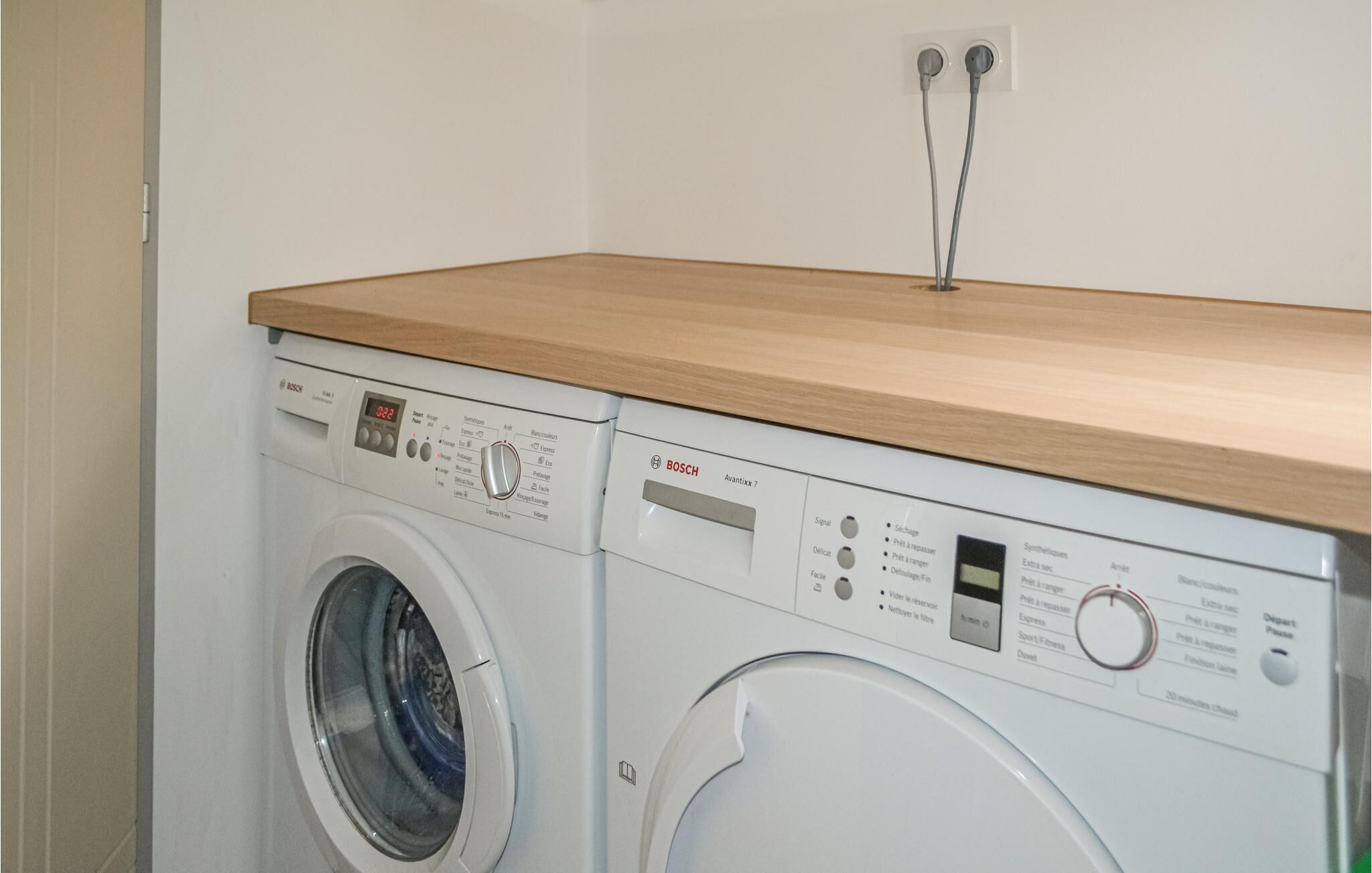 A front-loading Bosch washing machine with a wooden countertop above it.