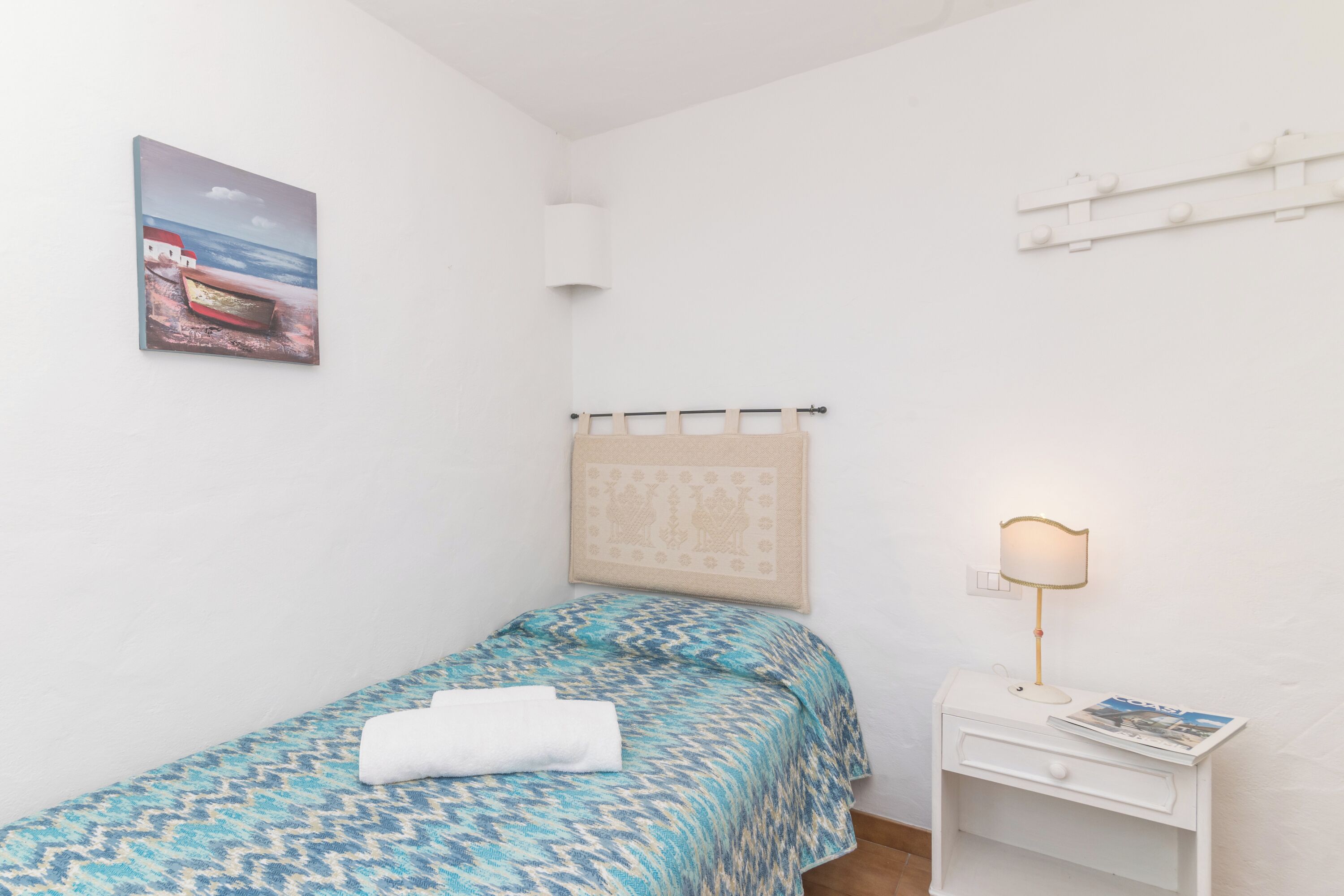 Una camera da letto piccola e ordinata, con una coperta a motivi, una lampada da comodino e un quadro appeso al muro.