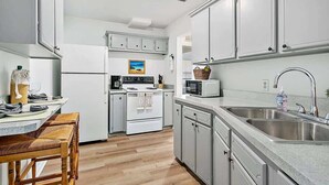 A modern kitchen with white cabinets, a microwave, a sink, and a wooden bench. - Orange Door Bungalow - Central, Cozy, 3BR (Jacksonville)