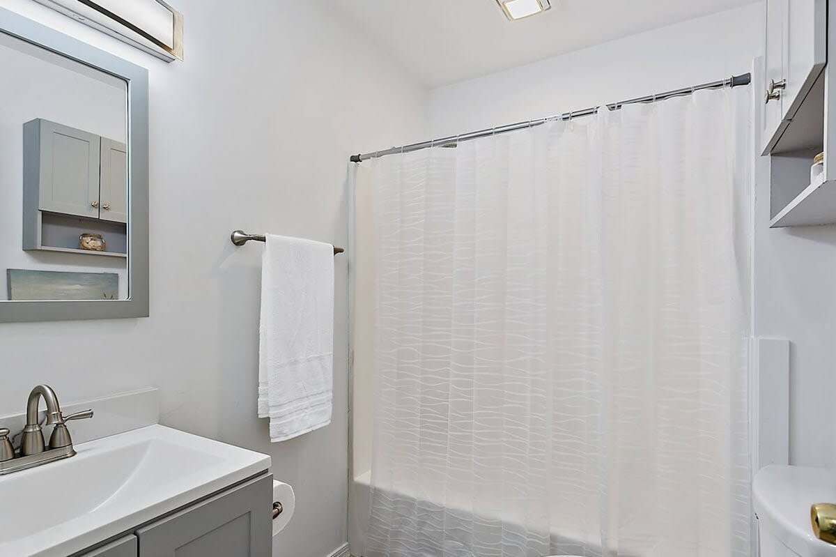 A bathroom with a white sink, a mirror, a towel rack, and a shower curtain.