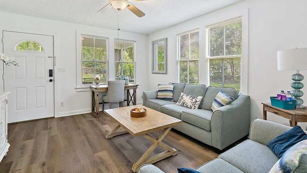 A well-lit living room with a ceiling fan, a sofa, a coffee table, and a dining area with a table and chairs. - Orange Door Bungalow - Central, Cozy, 3BR (Jacksonville)
