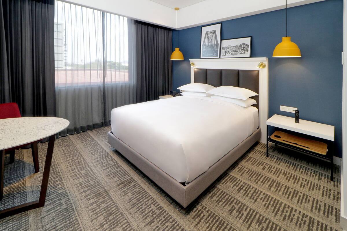 Una habitación de hotel con una cama grande, una mesita de noche, una silla y vistas al exterior por la ventana.