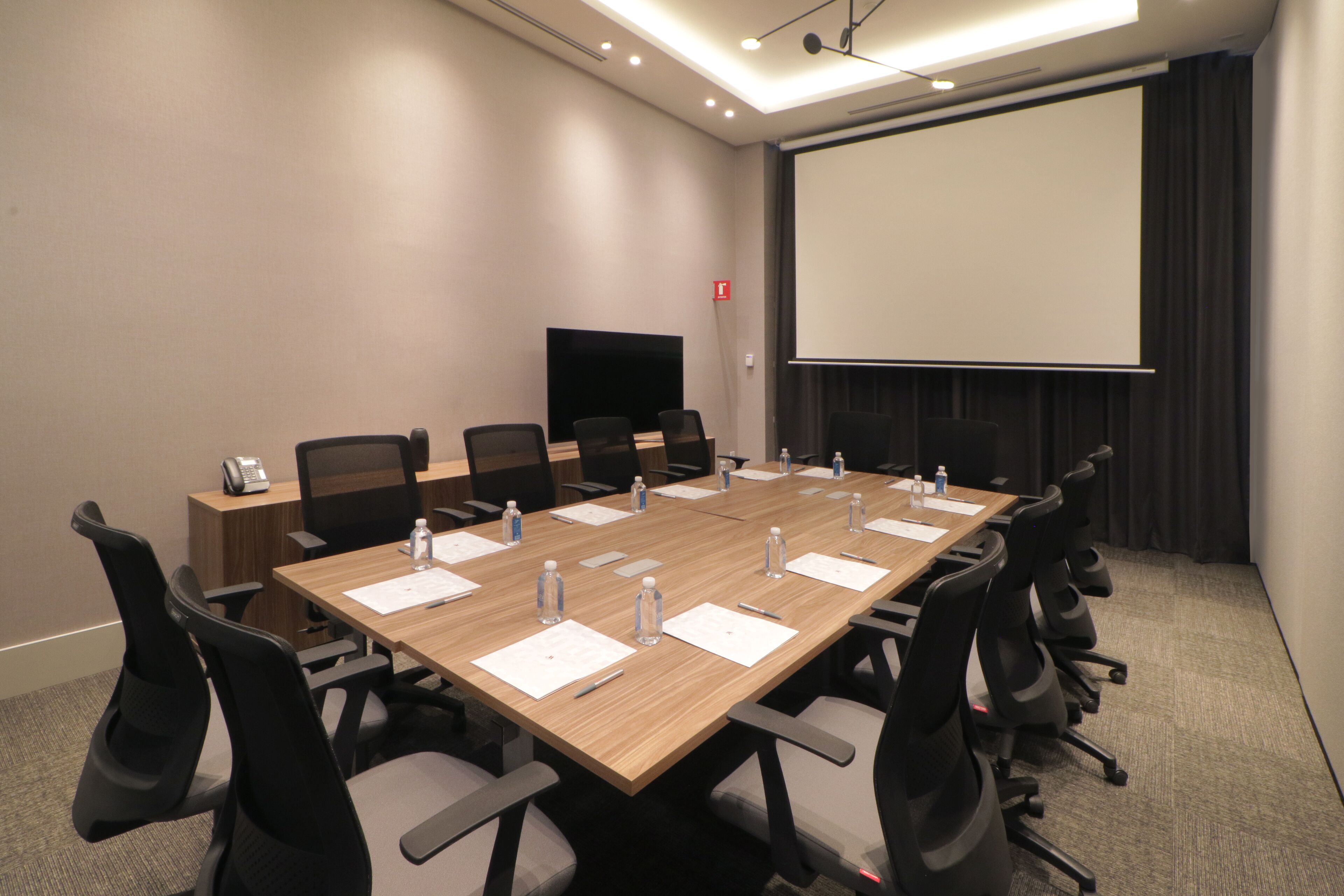 Una sala de conferències amb una taula llarga, cadires, una pantalla de projector i un televisor pla.