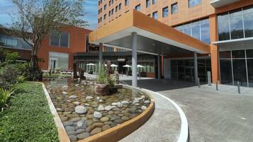 A modern building with a covered entrance, a landscaped garden with a pond, and a clear sky.