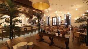 Un restaurante con mesas y sillas de madera, una zona de bar e iluminación decorativa.