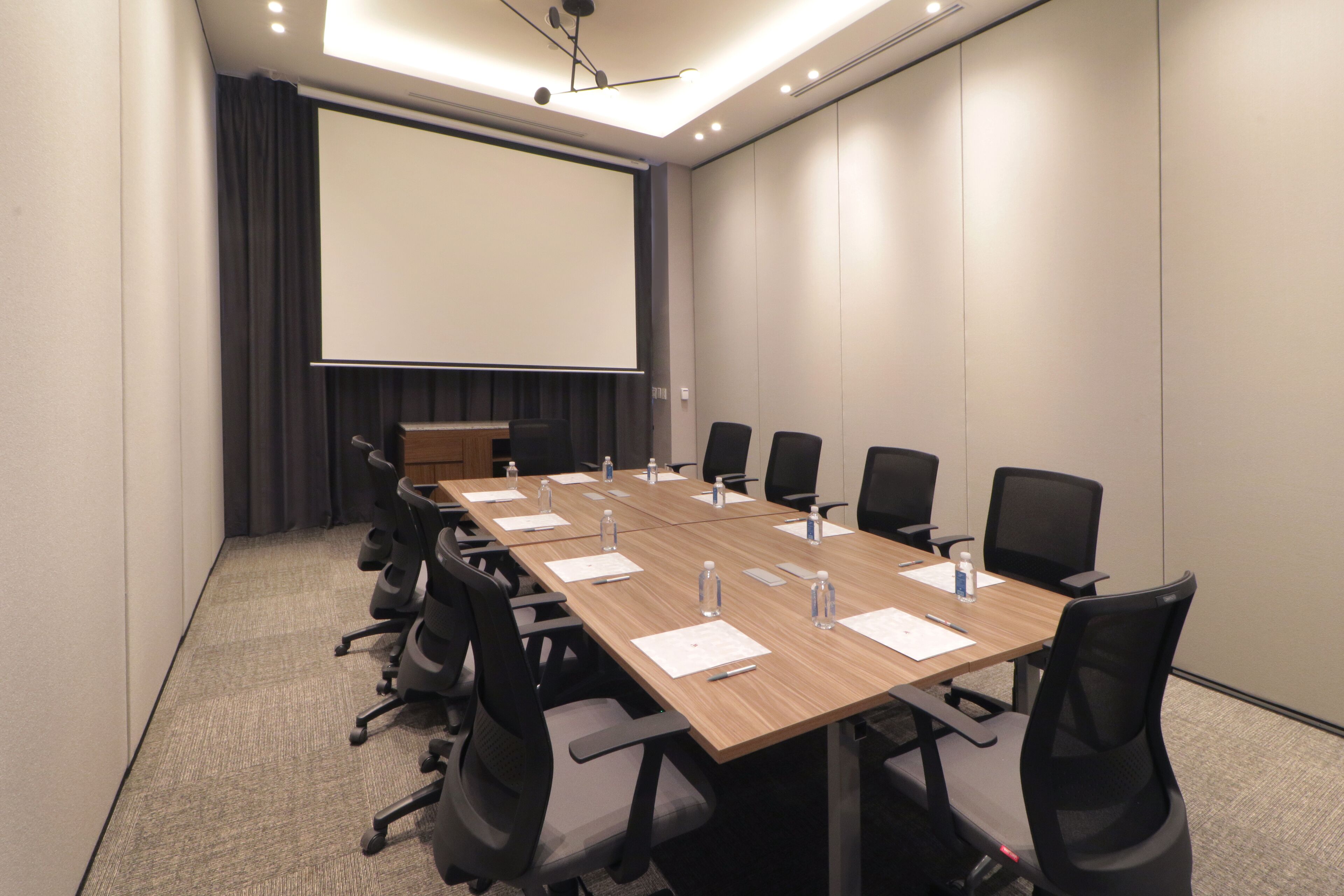 Un salón de conferencias con una larga mesa, sillas, una pantalla de proyector y un atril.