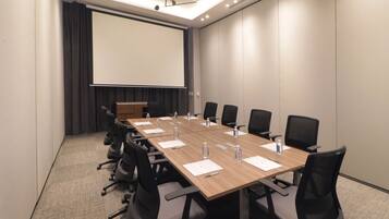 Un salón de conferencias con una larga mesa, sillas, una pantalla de proyector y un atril.