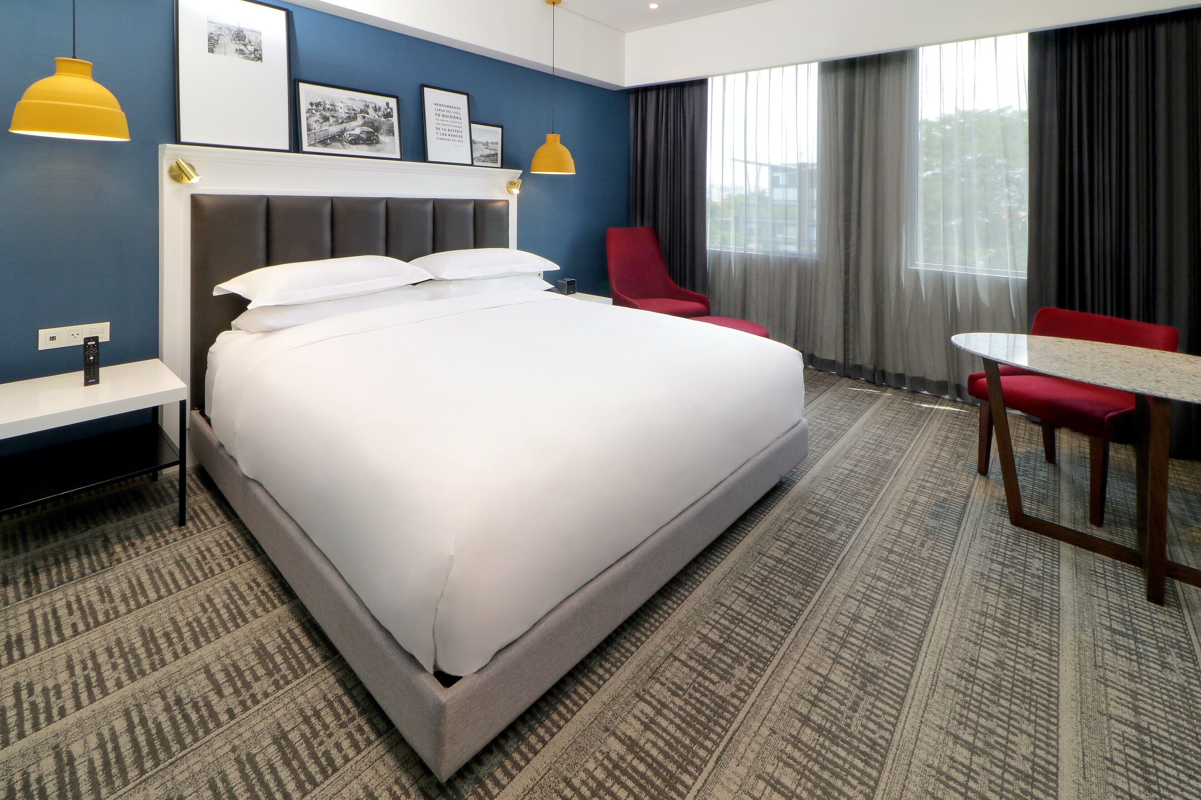 Una habitación de hotel con una cama grande, una silla roja, una mesita y una ventana con cortinas.