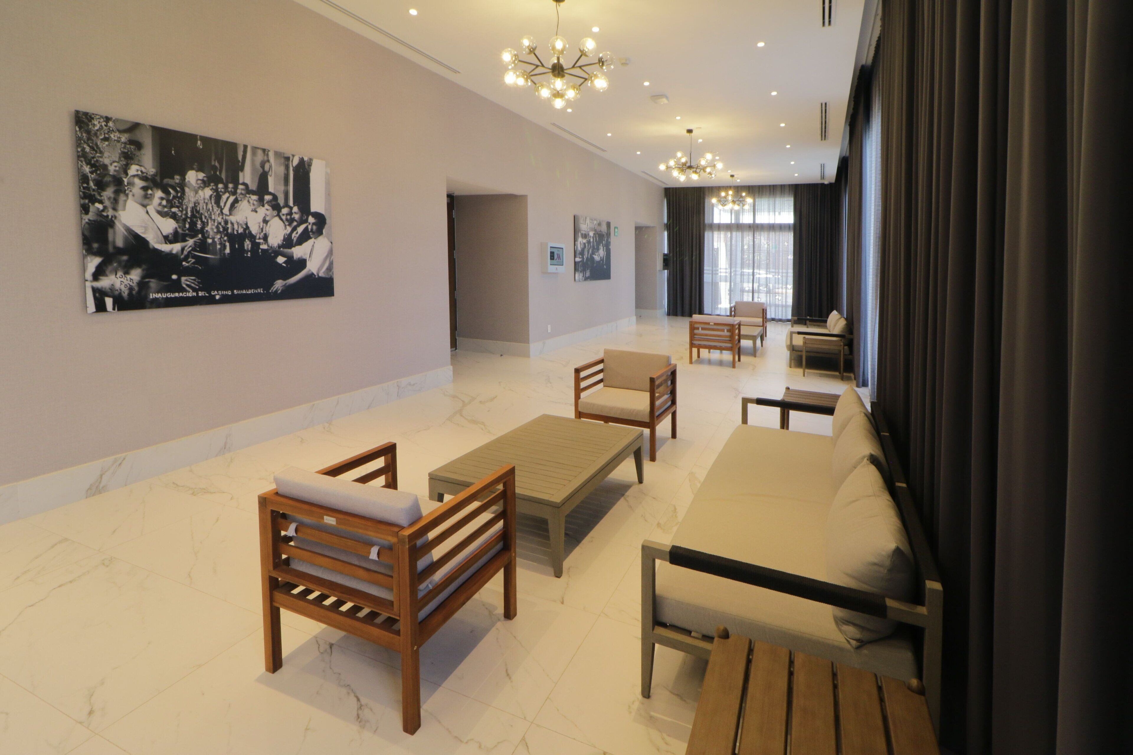 A spacious room with a large sofa, wooden chairs, a coffee table, and a dining table. There is a large black and white photograph on the wall and a chandelier hanging from the ceiling.