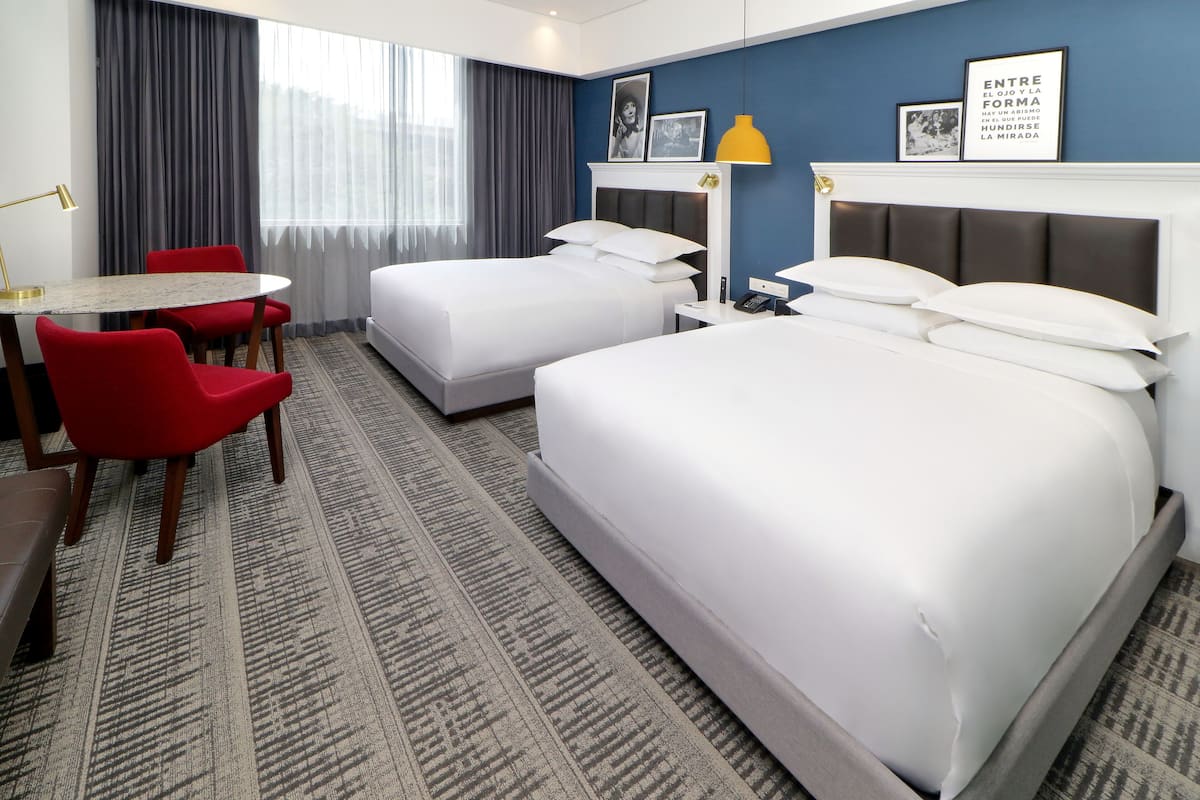 Habitación de hotel con dos camas, un escritorio, sillas rojas y una alfombra estampada.