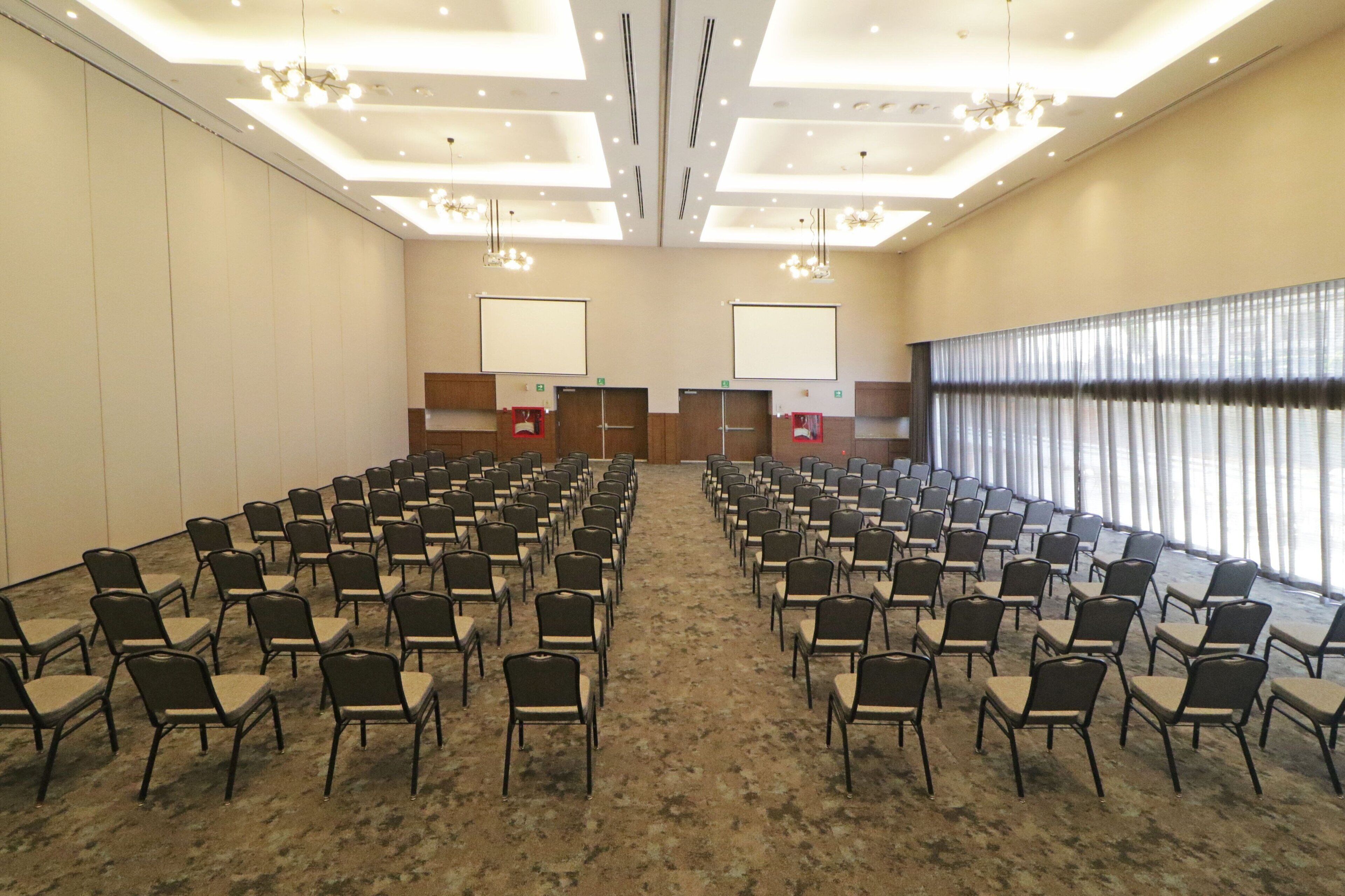 A conference room with rows of chairs, a podium, and a large window with curtains.