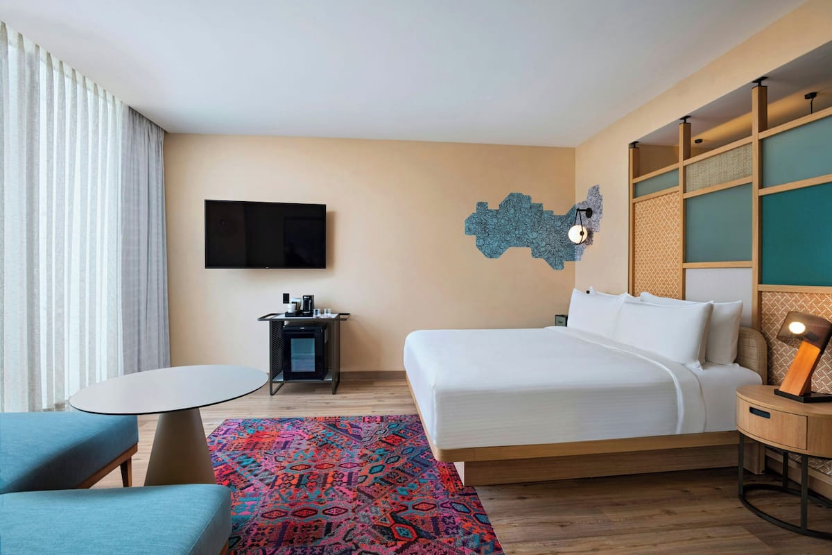 Une chambre d’hôtel avec un lit, un bureau, une chaise, une télévision et un tapis à motifs.