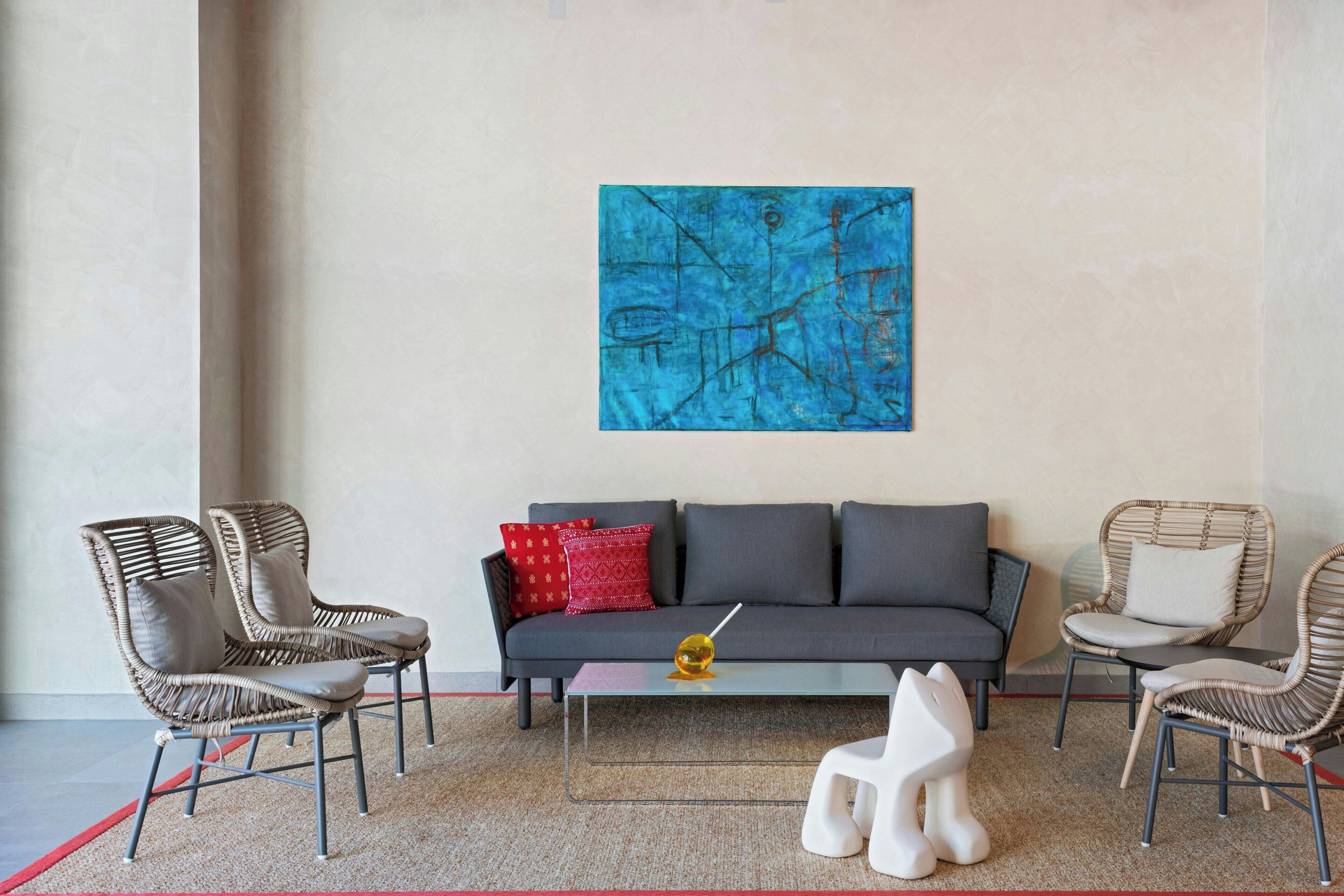 A modern living room with a grey sofa, wicker chairs, a glass coffee table, and a blue abstract painting on the wall.