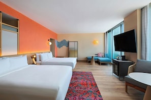 A hotel room with two beds, a TV, a sofa, a table, and a large window.