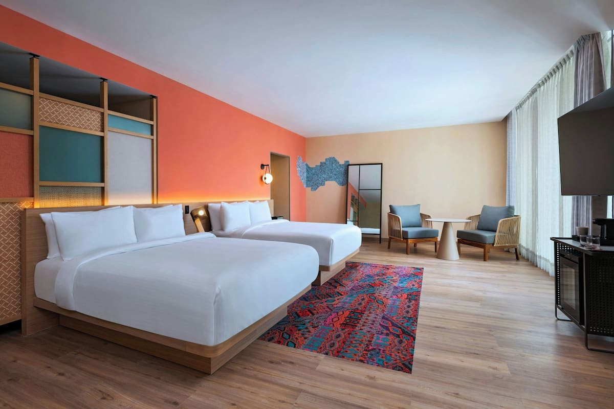 Une chambre d’hôtel avec deux lits, une petite table, une télévision et une grande fenêtre avec des rideaux.